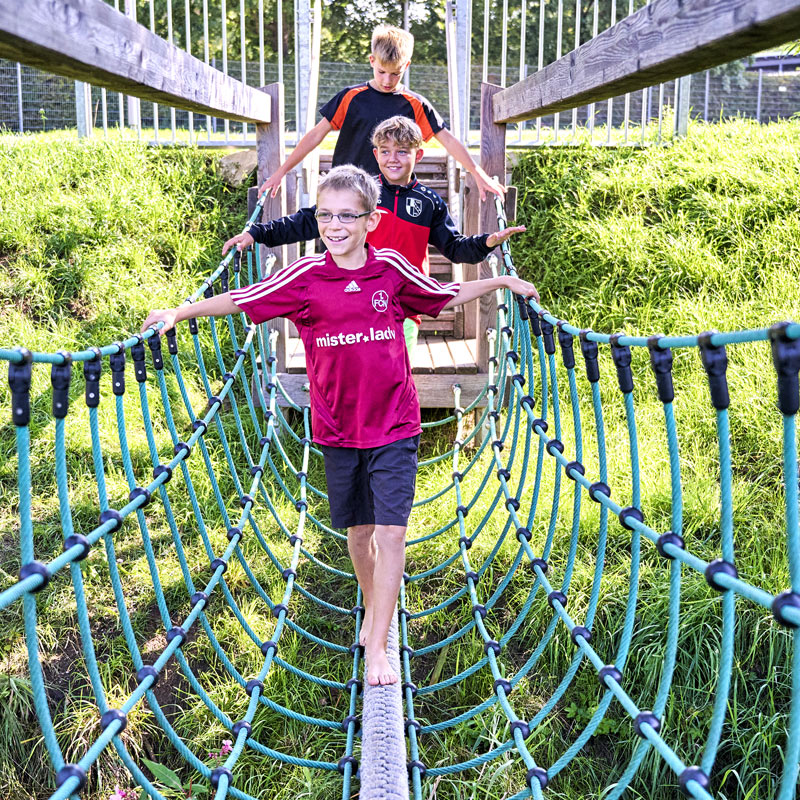 Mehrere Kinder laufen über eine Hängebrücke aus Seilen