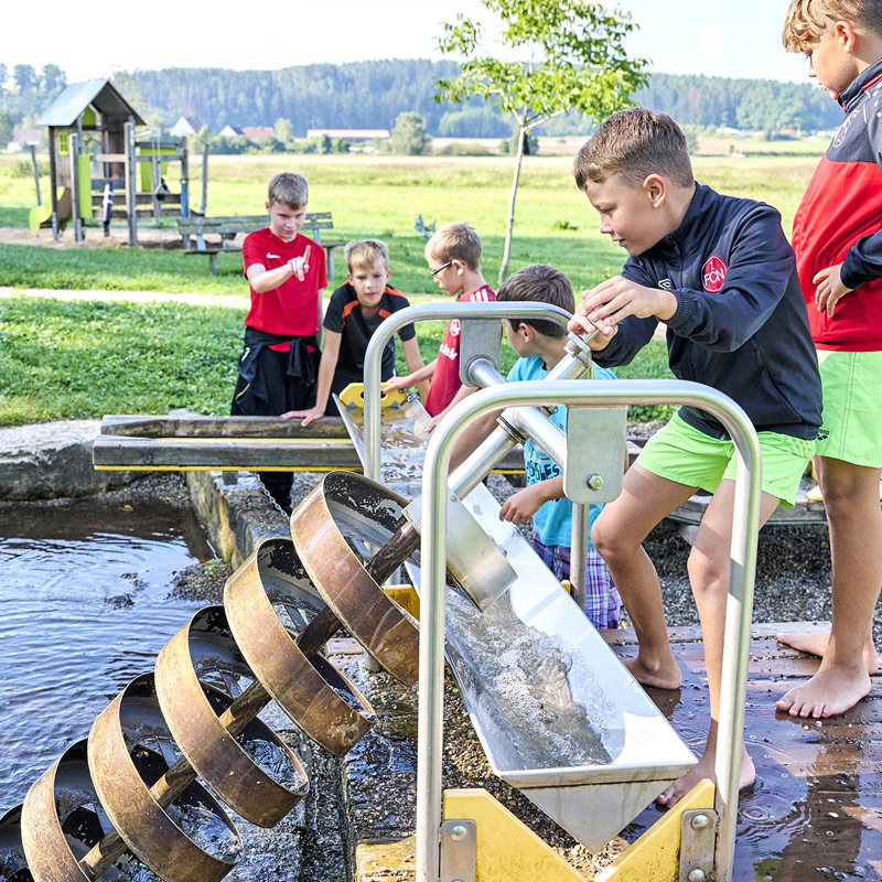 Kinder spielen mit einer Kurbelstation am Wasserspielplatz